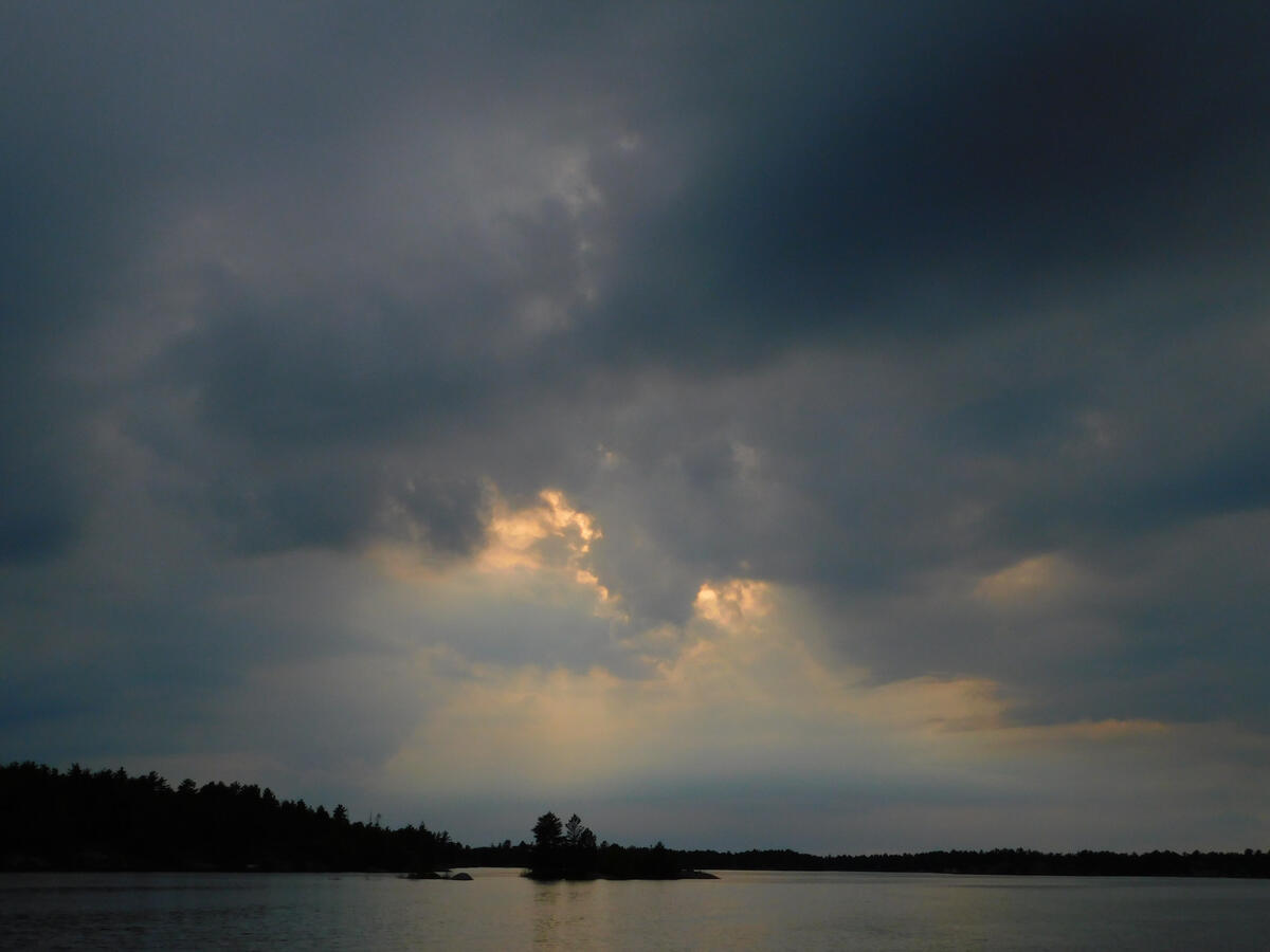A blue sky, with yellow rays of sun peeking though cloud cover. Shot in Ontario, Canada.